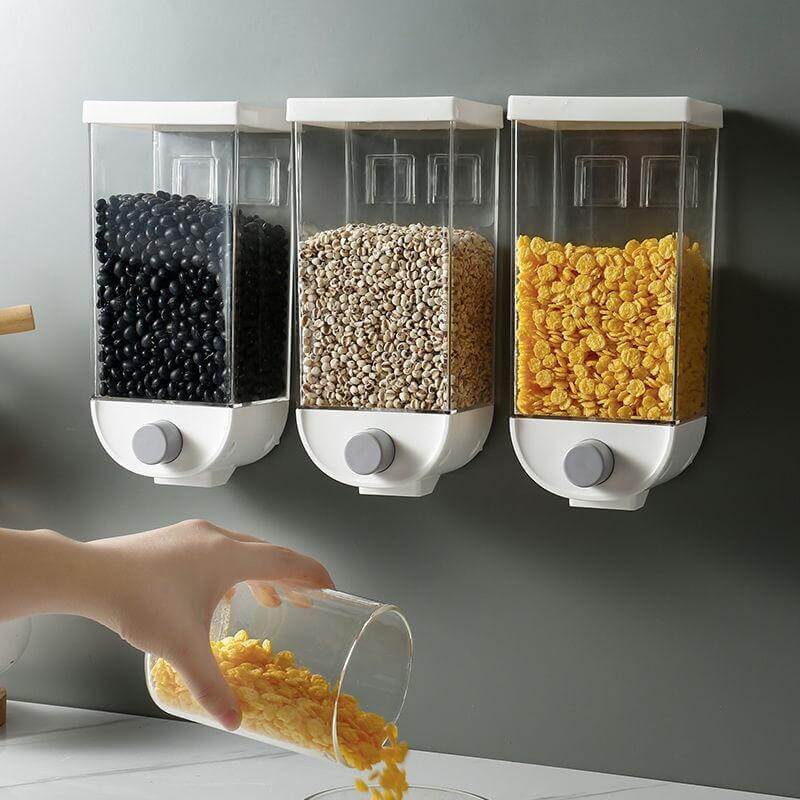 Three white wall mounted grain dispensers filled with black beans, oats, and corn flakes being used to pour cereal