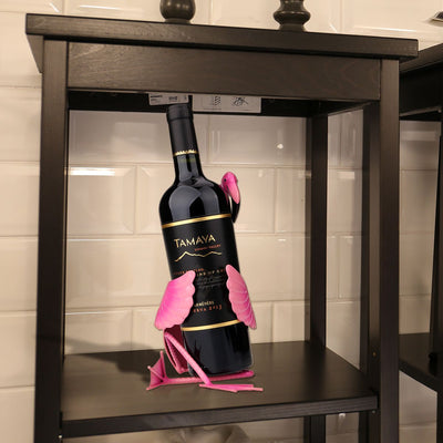 Pink flamingo wine holder shaped like a flamingo holding a wine bottle on a black shelf