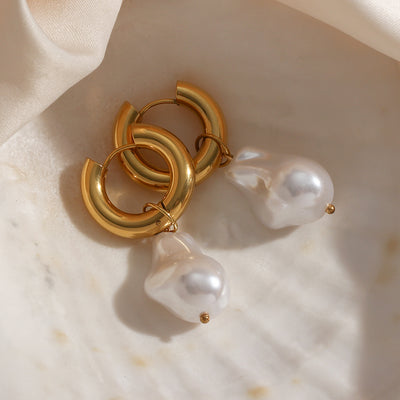 Elegant water drop earrings with gold hoop and large pearl drop design on marble surface