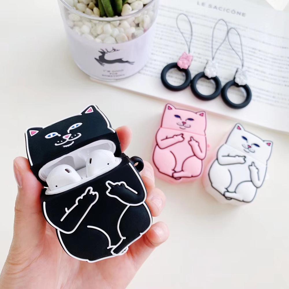 Hand holding black cartoon cat AirPods case with two other pink and white cartoon cat AirPods cases on table